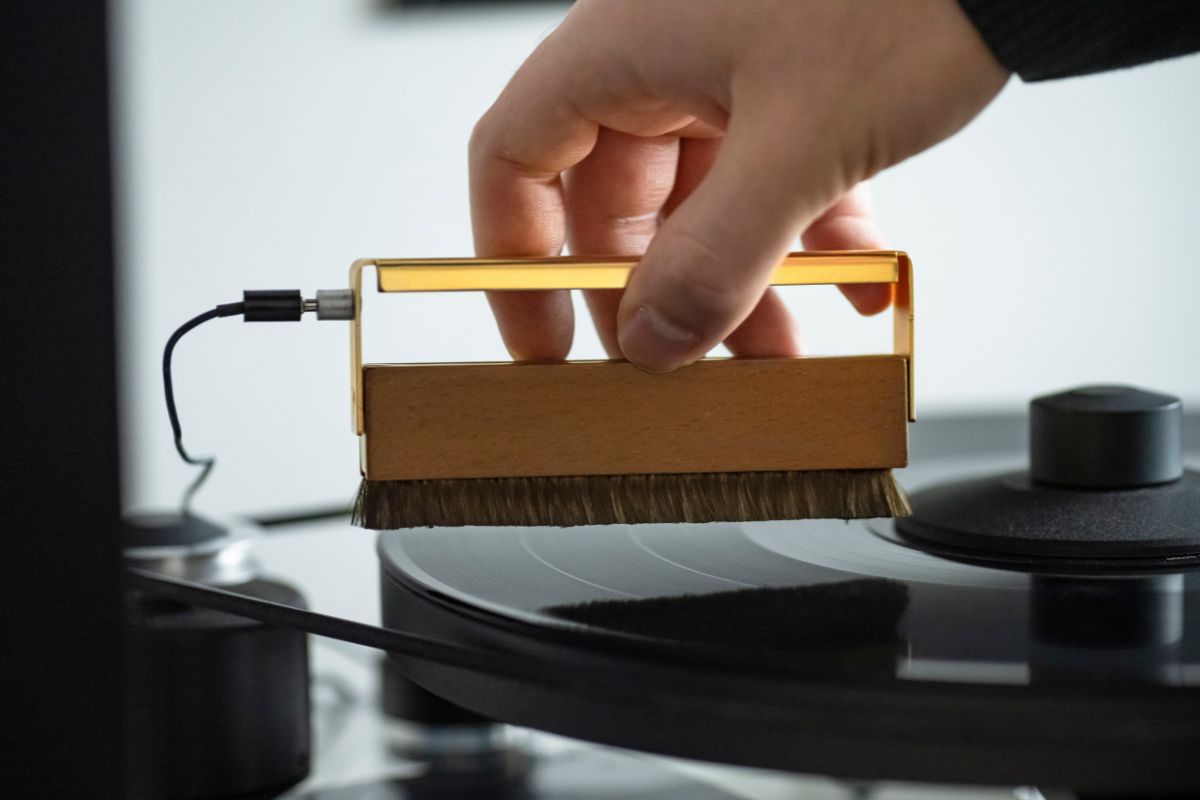 Hand reinigt eine Vinyl-Schallplatte mit einer antistatischen Carbonfaserbürste auf einem Plattenspieler.