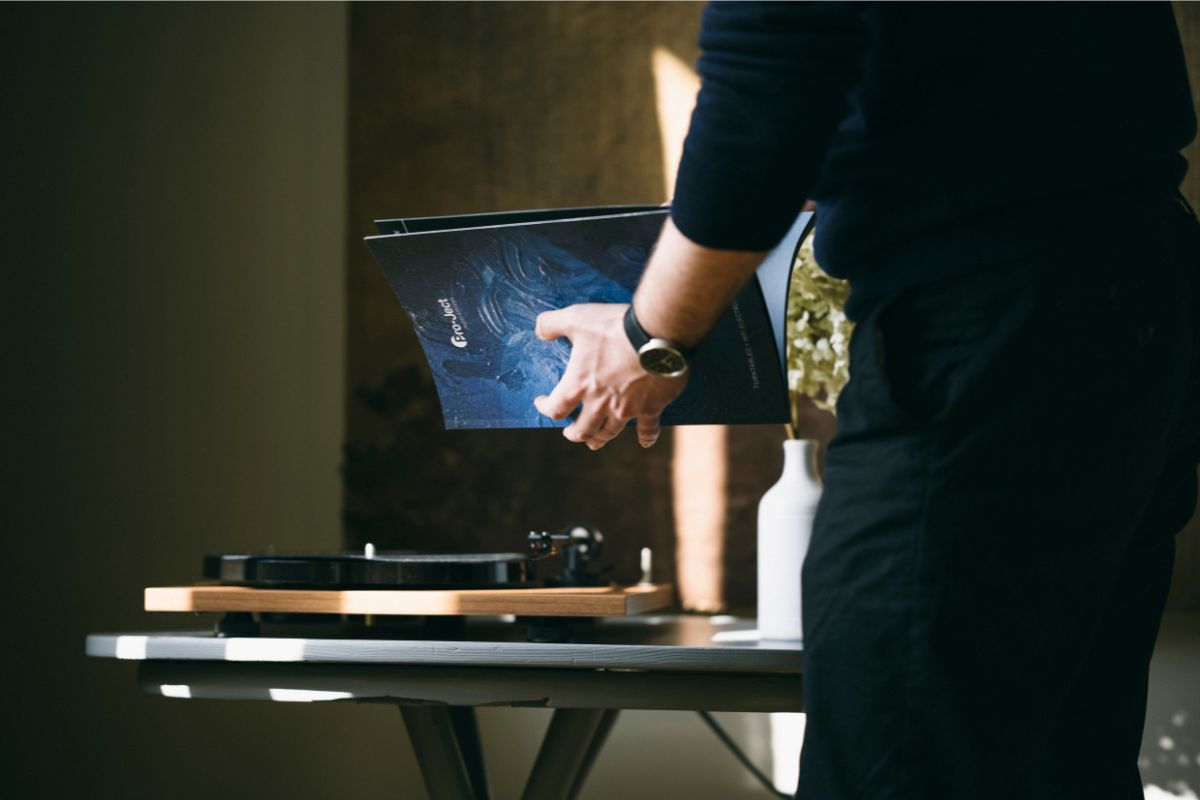 Person blättert in einer Pro-Ject-Anleitung, während ein Plattenspieler auf einem Tisch im Hintergrund steht.