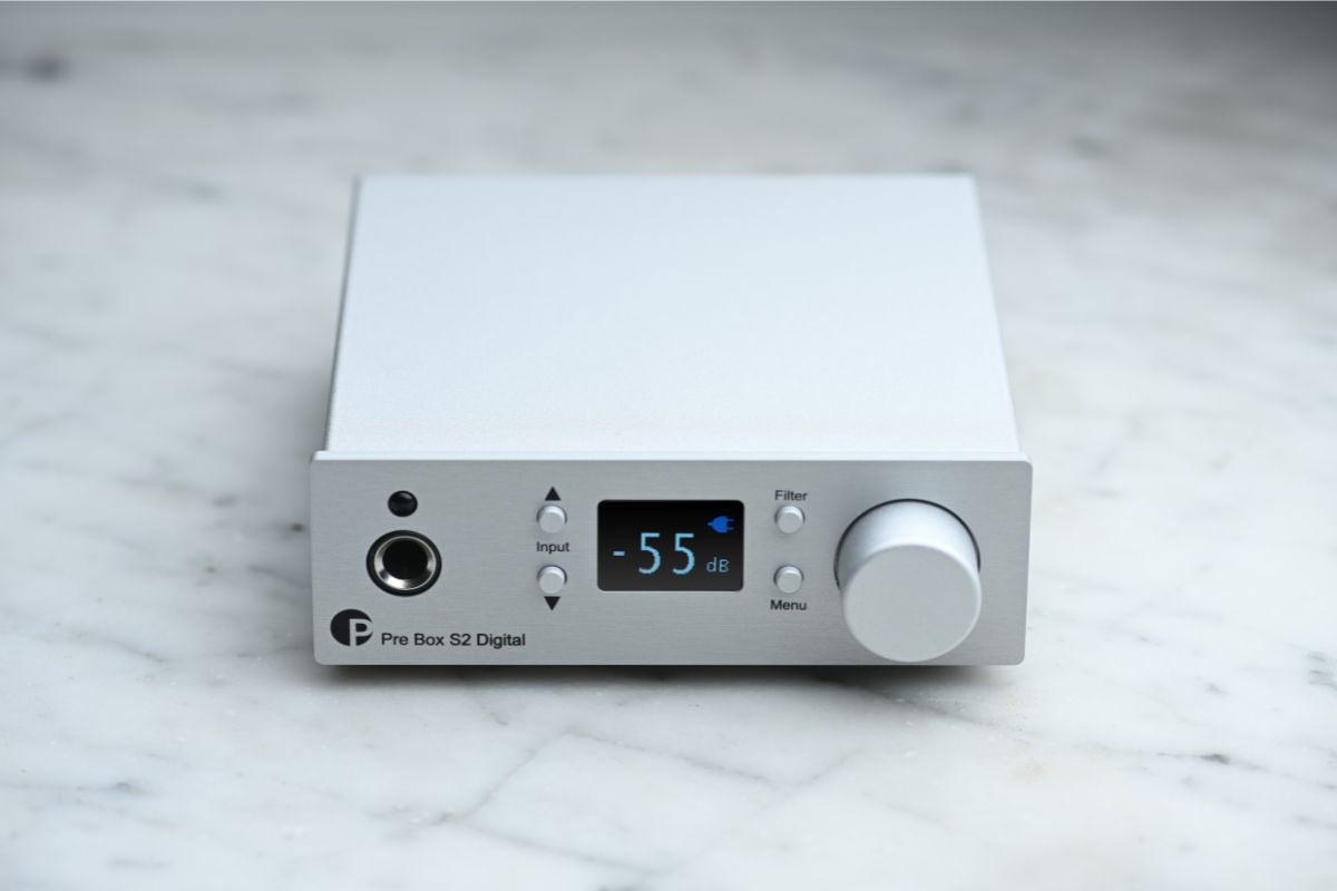 Kompakter digitaler Vorverstärker Pro-Ject Pre Box S2 Digital in silbernem Aluminiumgehäuse, frontal fotografiert auf einer hellen Marmoroberfläche mit beleuchtetem Display und Bedienelementen.