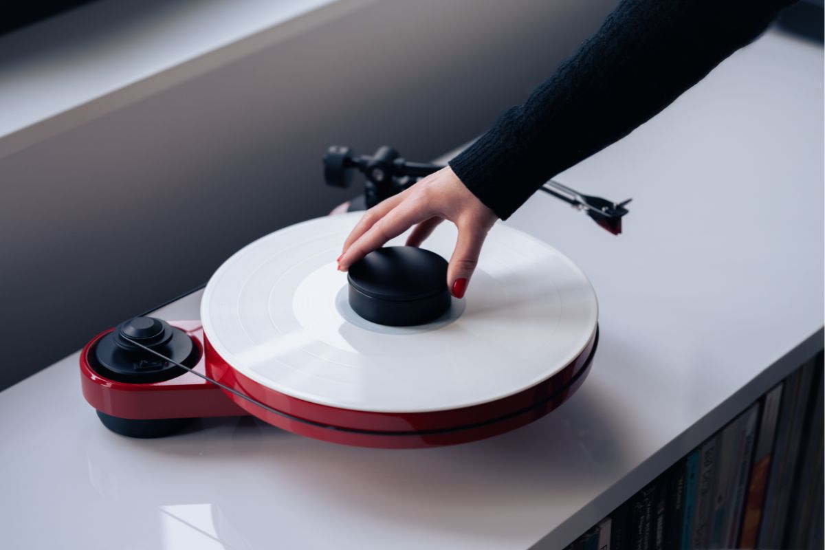 Hand legt einen schwarzen Plattenpuck auf einen weißen Plattenteller eines roten Plattenspielers, der auf einem Sideboard steht.