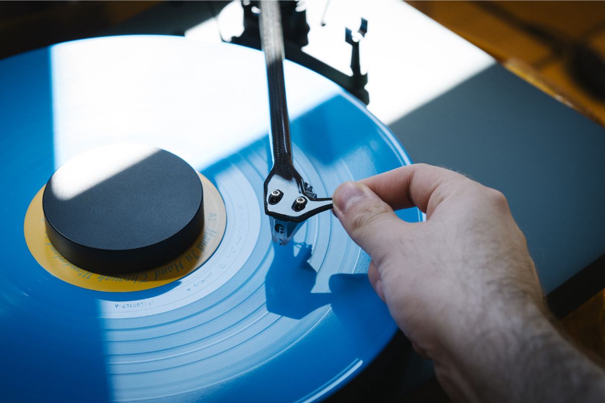 Hand setzt den Tonarm samt Nadel auf eine blaue Schallplatte