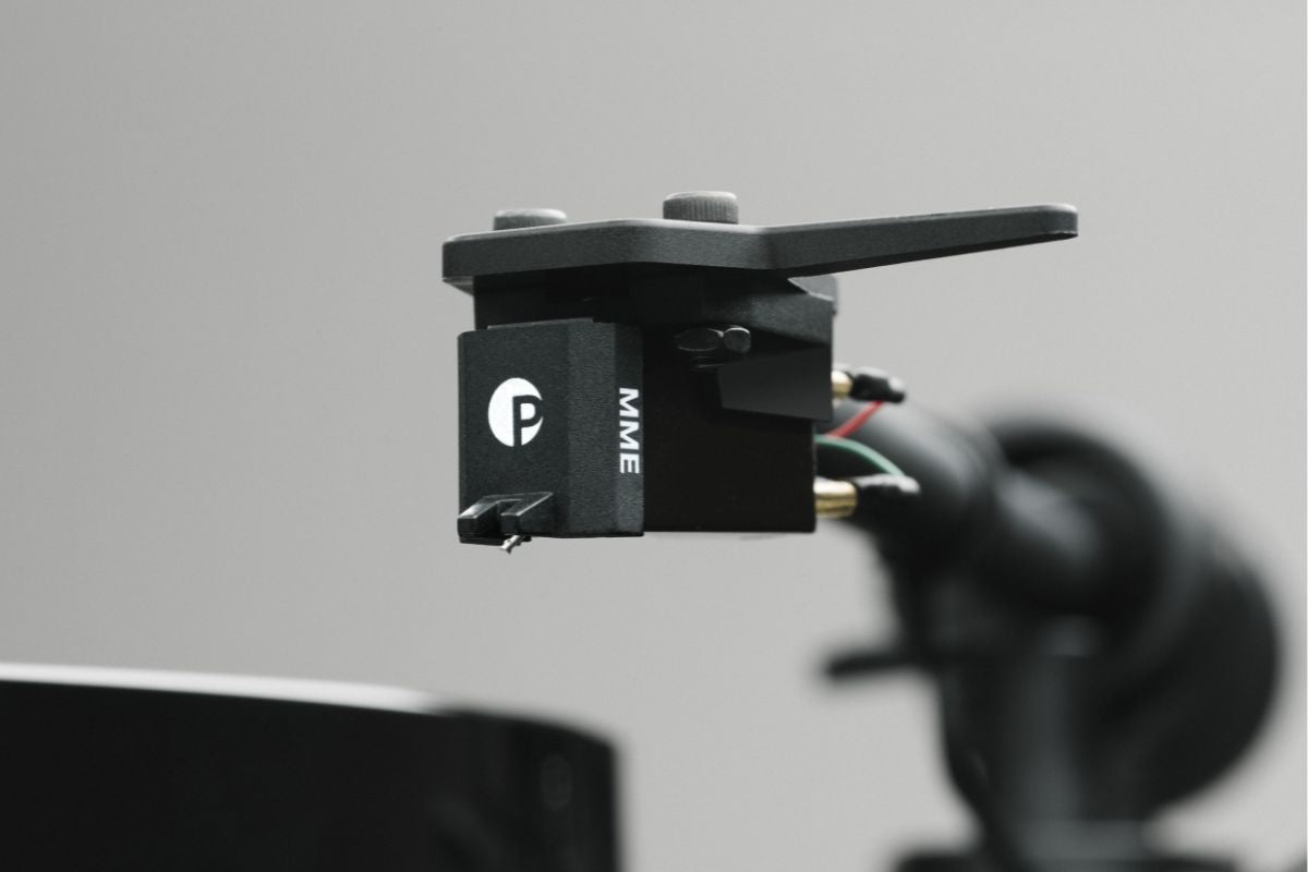 Nahaufnahme eines Pro-Ject MME-Tonabnehmers am Plattenspieler-Tonarm, vor neutral grauem Hintergrund.