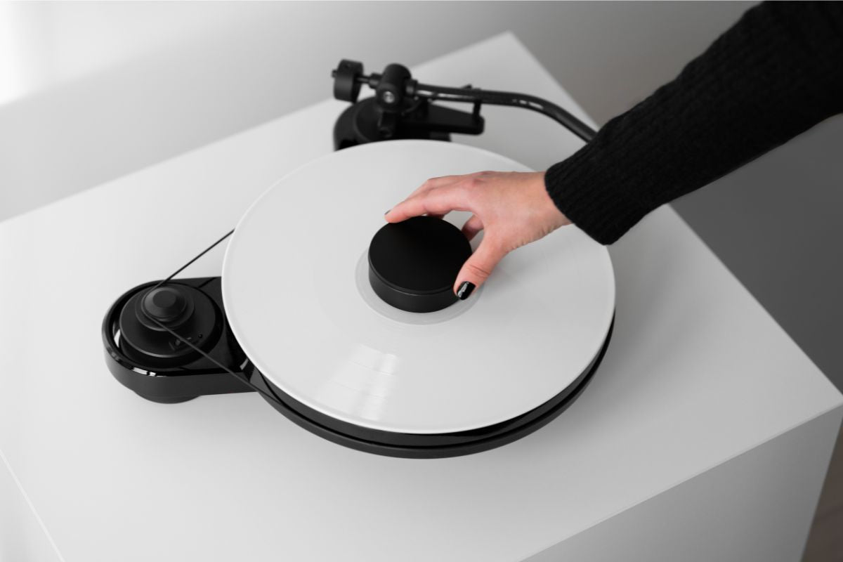 Hand legt einen schwarzen Plattenpuck auf eine weiße Schallplatte auf dem Plattenspieler;