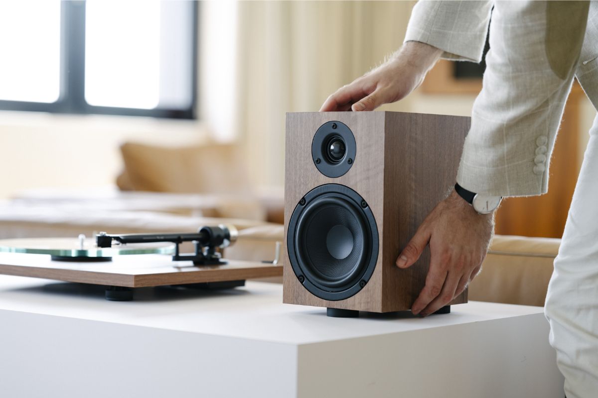 Person richtet einen kompakten Regallautsprecher aus Holzgehäuse auf einem Sideboard neben einem Plattenspieler aus