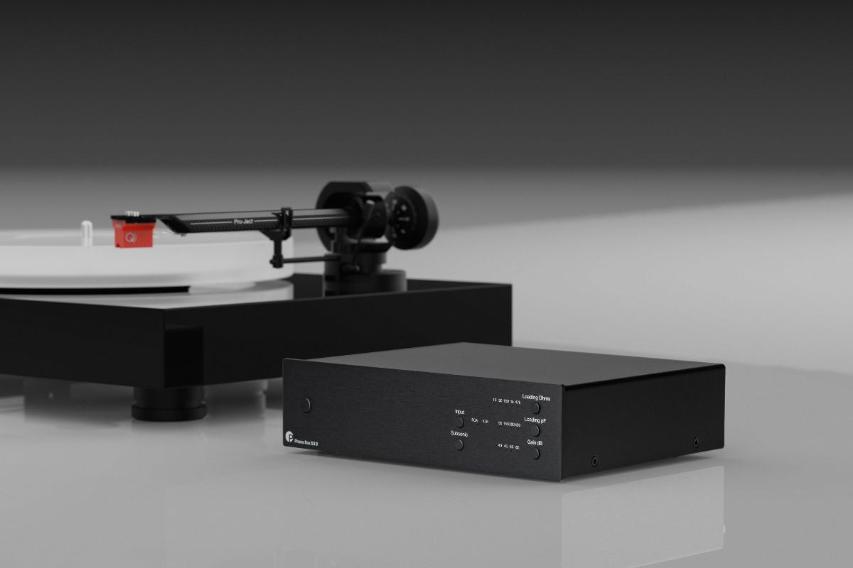 Schwarzer HiFi-Phonovorverstärker neben einem hochwertigen Plattenspieler mit montiertem Tonarm und rotem Tonabnehmer.